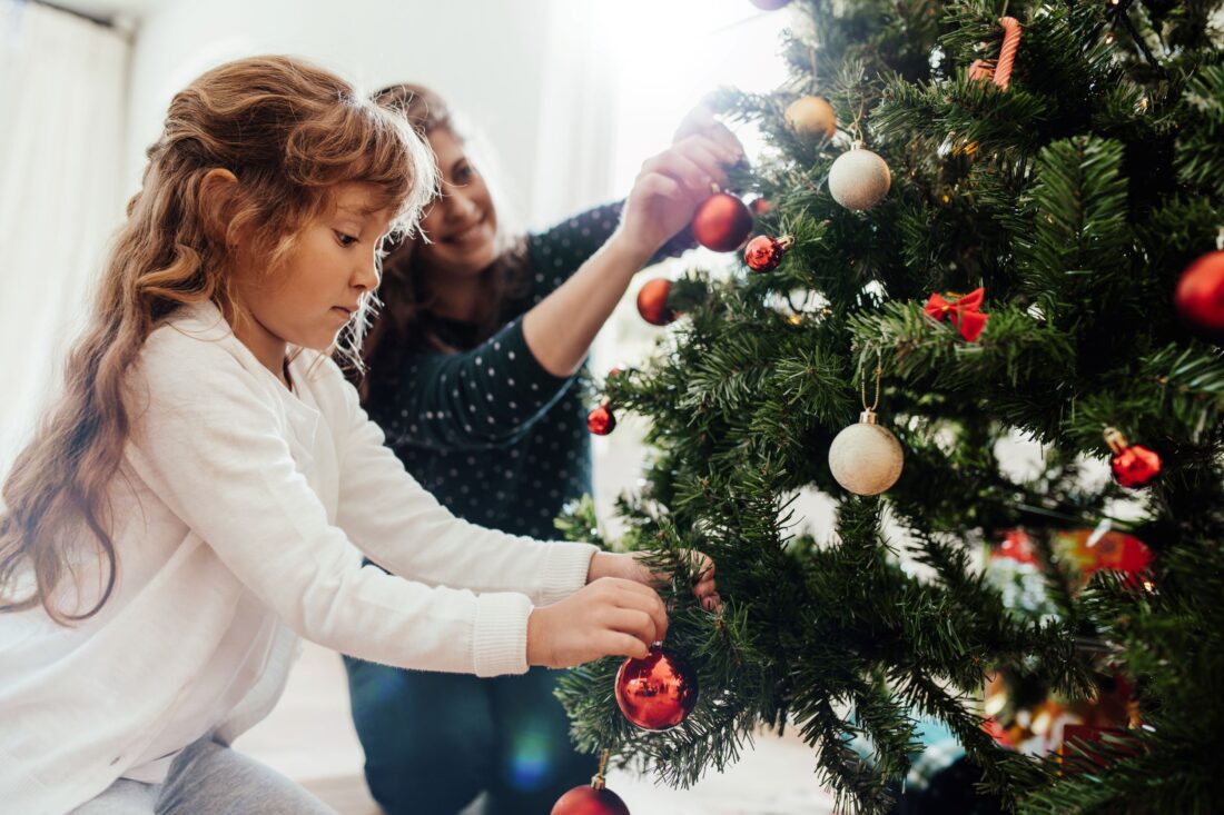 Árvore de Natal sendo decorada por criança e mãe.
